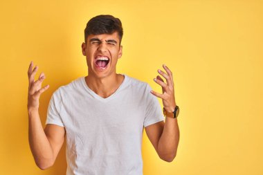İzole edilmiş sarı arka planda duran beyaz tişörtlü genç Hintli adam kollarını kaldırmış ve gözleri kapalı heyecanla haykırarak başarıyı kutluyor. Kazanan konsept