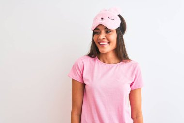 İzole edilmiş beyaz arka planda duran uyku maskesi takan genç ve güzel bir kadın yüzünde gülümsemeyle, doğal bir ifadeyle yan yana bakıyor. Kendinden emin gülen.