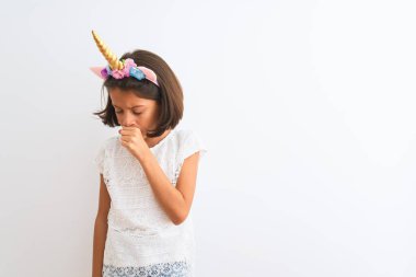 Tek boynuzlu at diademi takan güzel bir kız çocuğu izole edilmiş beyaz arka planda kendini iyi hissetmiyor ve soğuk algınlığı veya bronşitin belirtisi olarak öksürüyor. Sağlık hizmetleri kavramı.