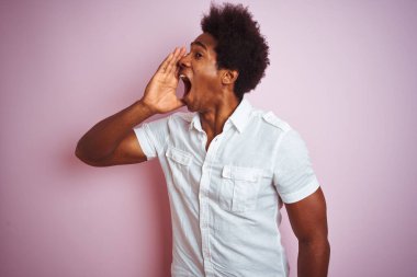 Afro saçlı, beyaz tişörtlü genç bir Amerikalı izole edilmiş pembe arka planda durup el ele tutuşarak bağırıyor ve bağırıyordu. İletişim konsepti.