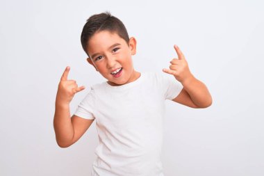 Güzel çocuk, izole edilmiş beyaz arka planda dikilmiş tişört giymiş çılgın bir ifadeyle elleri havada rock sembolü yaparak bağırıyor. Müzik yıldızı. Ağır konsept.