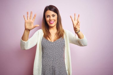 Pembe soyutlanmış arka planda duran genç ve güzel bir kadın sekiz numaralı parmaklarıyla gülümseyerek kendinden emin ve mutlu bir şekilde işaret ediyor..