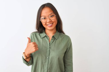 Yeşil tişörtlü ve gözlüklü genç Çinli bir kadın izole edilmiş beyaz arka planda mutlu bir el hareketi yapıyor. Kameraya bakıp başarıyı gösteren ifade onaylanıyor.