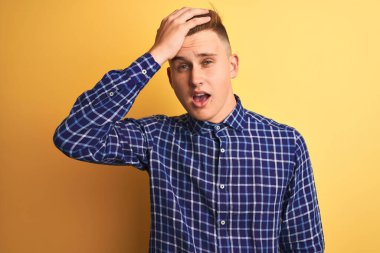 İzole edilmiş sarı arka plan üzerinde duran sıradan tişörtlü genç ve yakışıklı bir adam. Hatayla el ele tutuşarak şaşırdı. Hatayı hatırla. Unuttum, kötü hafıza konsepti.