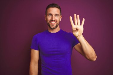 Leylak renginde günlük mor tişört giyen genç adam arka planda kendini beğenmiş ve mutlu bir şekilde gülümserken dört numarayı işaret ediyor..