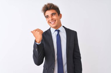 İzole edilmiş beyaz arka planda duran takım elbiseli genç ve yakışıklı işadamı gülümsüyor ve başparmağıyla yan tarafa bakıyor..