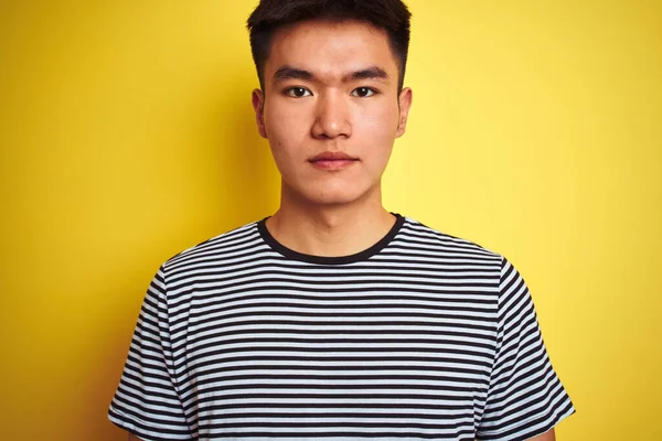 若いですアジアの中国人男性身に着けていますストライプTシャツ上に立って隔離された黄色の背景に自信を持って表現上のスマート顔真剣に考えて — ストック写真