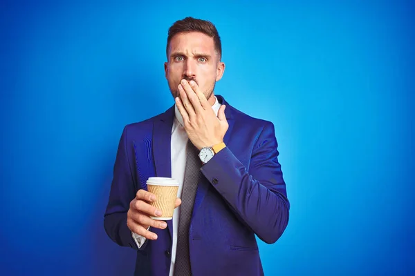 Young handsome business man drinking a coffee on a paper cup over blue isolated background cover mouth with hand shocked with shame for mistake, expression of fear, scared in silence, secret concept