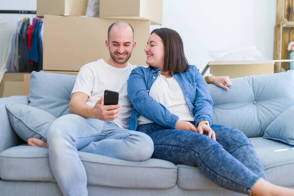Молода пара сидить на дивані в новому будинку, використовуючи смартфон — стокове фото