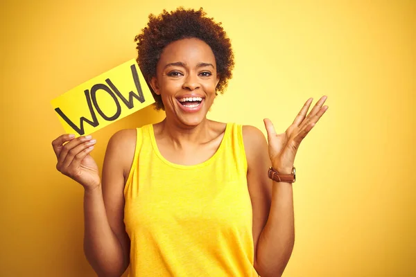 Young african american woman showing wow banner board over yellow isolated background very happy and excited, winner expression celebrating victory screaming with big smile and raised hands