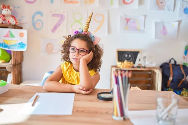 漂亮的幼儿戴着眼镜 骑着独角兽日记 坐在幼儿园的课桌上 满脑子疲惫 双手交叉 对抑郁症感到厌烦 — 图库照片