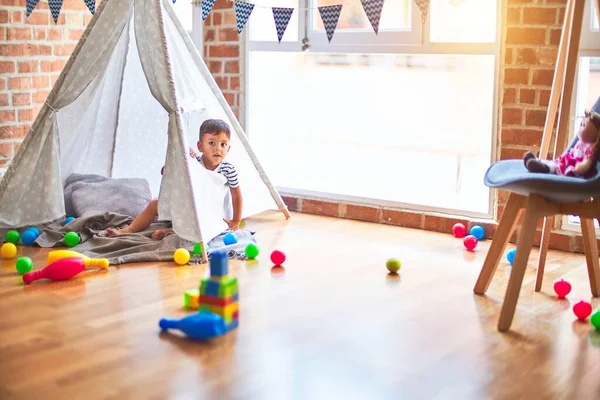 Beautiful toddler boy sitting on the floor playing inside  tipi at kindergarten