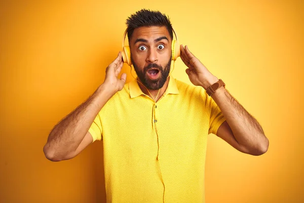 驚きの顔 恐怖と恐怖の表現で興奮してショックで怖がって孤立した黄色の背景の上にヘッドフォンを使用して音楽を聞いてアラブインドのヒスパニック男 — ストック写真