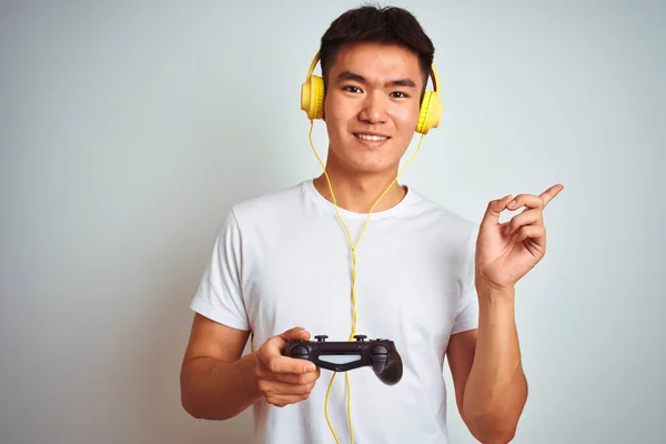 年轻的亚裔中国游戏玩家玩电子游戏时 站在与世隔绝的白色背景上 很高兴手指手画脚地指向旁边 — 图库照片