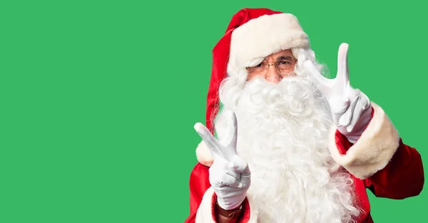 中年英俊男子身穿圣诞老人服装 蓄着胡子 站在那里笑着 伸出双手的手指做胜利的标志 第二点 — 图库照片