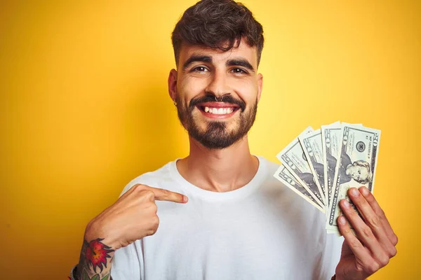 Νεαρός Άνδρας Τατουάζ Κρατώντας Δολάρια Στέκεται Πάνω Από Απομονωμένο Κίτρινο — Φωτογραφία Αρχείου