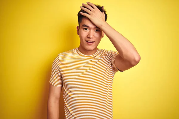 若いアジアの中国人男性のTシャツを着て孤立した黄色の背景の上に立ってミスのための頭の上に手で驚いて エラーを覚えている 忘れられた悪い記憶の概念 — ストック写真