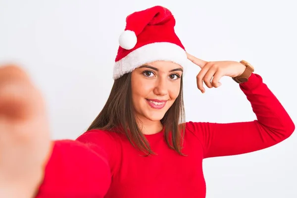 戴着圣诞圣诞圣诞礼帽的女孩在与世隔绝的白色背景上用相机自拍 她非常高兴地用手和手指指指点点 — 图库照片