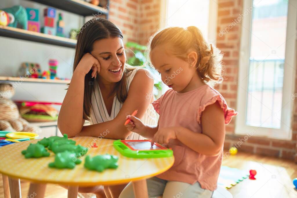 Beautiful teacher and blond student toddler girl drawing using digital board at kindergarten