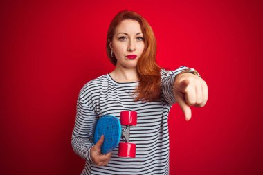 Kızıl saçlı genç bir kız, kırmızı arka planda paten kayıyor. Kamerayı işaret ediyor. Ve sen, el işareti, ön taraftan pozitif ve kendinden emin bir hareket.