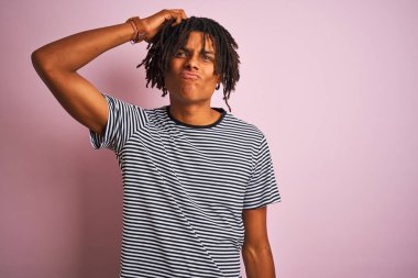 Rasta desenli tişörtlü Afro bir adam izole edilmiş pembe arka plan kafa karışıklığı ve soru sorulmasını bekliyor. Şüpheyle kararsız, kafa kafaya düşünerek. Düşünceli kavram.