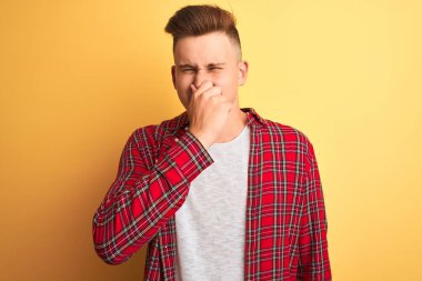 Sarı arka planda duran sıradan bir tişört giymiş genç yakışıklı bir adam pis ve iğrenç bir koku alıyor. Dayanılmaz bir koku. Parmakları burnunda nefesini tutuyor. Kötü koku konsepti.