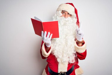 Noel Baba kostümü giyen orta yaşlı bir adam izole edilmiş beyaz arka plan üzerine kitap okuyor üzgün ve üzgün görünüyor, parmaklarıyla yönü gösteriyor, mutsuz ve depresif..