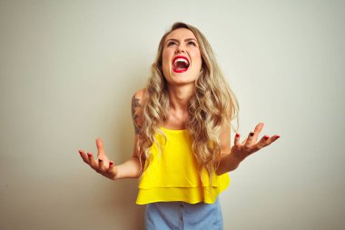 Beyaz izole arka plan üzerinde duran sarı t-shirt giyen genç güzel kadın deli ve deli bağırarak ve agresif ifade ve kollar kaldırdı ile bağırıyor. Hayal kırıklığı kavramı.