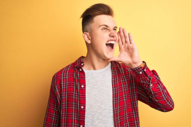 Sarı arka planda dikilip el ele tutuşarak bağıran genç ve yakışıklı bir adam. İletişim konsepti.