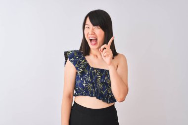 Yazlık çiçekli tişört giyen genç, güzel Çinli bir kadın izole edilmiş beyaz arka plan üzerinde başarılı bir fikirle işaret ediyor. Heyecanlı ve mutlu. Bir numara..