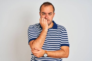 İzole edilmiş beyaz arka plan üzerinde duran sıradan çizgili polo giyen genç adam elleri ağız yiyen tırnaklarla gergin ve stresli görünüyor. Endişe sorunu.