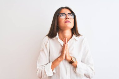 Gözlüklü genç ve güzel bir iş kadını, izole edilmiş beyaz arka planda duruyor. Elleriyle yalvarıyor ve dua ediyor. Yüzünde umut ifadesi var. Af diliyor. Din kavramı.