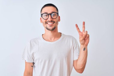 Gözlük takan ve izole edilmiş arka planda duran genç yakışıklı adam kameraya bakıp gülümsüyor ve zafer işareti yapıyor. İki numara..