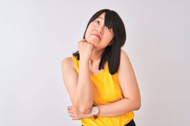 İzole edilmiş beyaz arka plan üzerine sarı tişört giyen genç, güzel Çinli kadın çenesi üzerinde soru soran, düşünceli bir ifade takınıyor. Düşünceli bir yüzle gülümsüyor. Şüphe kavramı.