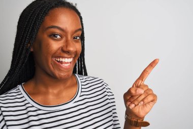 Genç Afro-Amerikalı kadın çizgili tişört giyiyor. İzole edilmiş beyaz arka planda duruyor. Elleri ve parmakları kenarda mutlu bir şekilde duruyor.