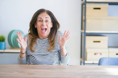 Orta yaş kıdemli kadın evde masada oturan çılgın kutluyor ve başarı için hayran silah kaldırdı ve açık gözleri heyecanlı çığlık. Kazanan kavramı