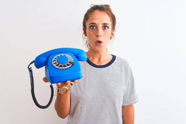 Genç kızıl saçlı kadın klasik retro telefonu izole edilmiş arka planda tutuyordu. Şaşırmış bir yüzle korkmuş ve korku ifadesinden korkmuştu.