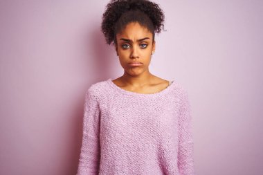Kışlık kazak giyen genç Afro-Amerikalı kadın pembe arka planda dikiliyor depresif ve endişeli, sinirli ve korkmuş. Üzücü ifade.