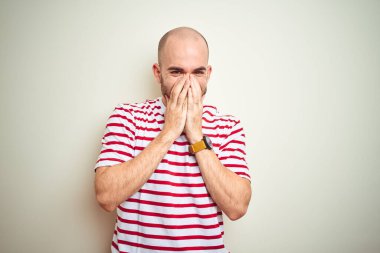 Sakallı genç ve kel bir adam, beyaz izole edilmiş arka planda günlük kırmızı tişört giyiyor. Gülüyor ve kıkırdıyor. Ağzı ellerle, dedikoduyla ve skandal konseptiyle örtüyor.