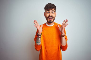 Turuncu süveter giyen genç adam, izole edilmiş beyaz arka planda duruyor. Çılgınlığı kutluyor ve başarı için hayrete düşüyor. Kolları havada ve gözleri açık, heyecanlı bir şekilde çığlık atıyor. Kazanan konsept