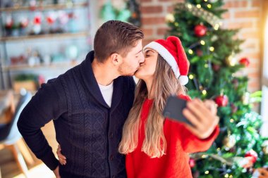 Mutlu ve kendinden emin gülümseyen genç bir çift. Sarılma ve öpüşme, evde Noel ağacının etrafında kamerayla selfie çektirir.