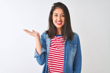 İzole edilmiş beyaz arka plan üzerinde çizgili t-shirt ve kot gömlek giyen genç Çinli kadın neşeli bir şekilde sunum yapıyor ve avuç içi kameraya bakıyor..