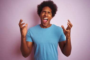 Afro saçlı, mavi tişörtlü Afro-Amerikalı bir adam izole edilmiş pembe arka planda duruyor ve başarıyı kutluyor. Kollarını kaldırıp, gözlerini kapatarak heyecanla haykırıyor. Kazanan konsept
