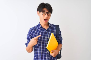 Sırt çantası taşıyan Çinli bir öğrenci izole edilmiş beyaz arka planda defter tutuyor. Elle ve parmakla işaret ederek çok mutlu.