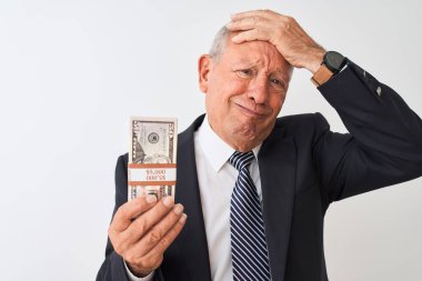Gri saçlı kıdemli işadamı, izole edilmiş beyaz arka planda dolar tutan takım elbiseli, elleri tetikte, utanç ve şaşkınlık dolu, sinirli ve hayal kırıklığına uğramış bir halde. Hata için korku ve üzüntü.