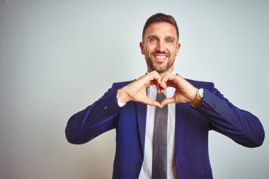 Genç ve yakışıklı bir iş adamı, izole edilmiş beyaz bir arka planda. Aşkla gülümsüyor. Elleriyle kalp sembolü ve şekli gösteriyor. Romantik konsept.