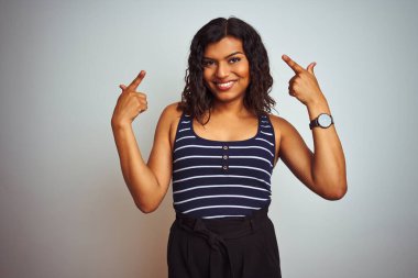 İzole edilmiş beyaz arka plan üzerinde çizgili tişört giyen transseksüel kadın gülümsemesi iki eliyle başını işaret ediyor, harika fikir ya da düşünce, iyi hafıza