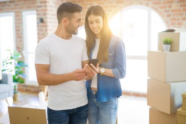 Genç çift yeni bir eve taşınıyor, akıllı telefon kullanarak gülümseyen ver