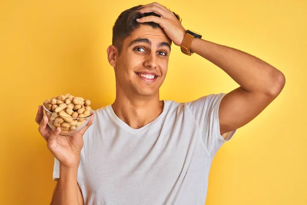 Young Indian Man Holding Bowl Peanuts Isolated Yellow Background Stressed — Stock Photo, Image