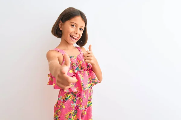 ピンクの花のドレスを着た若い美しい子供の女の子は 幸せと面白い顔を持つカメラに指を指して孤立した白い背景の上に立っている 良いエネルギーと振動 — ストック写真